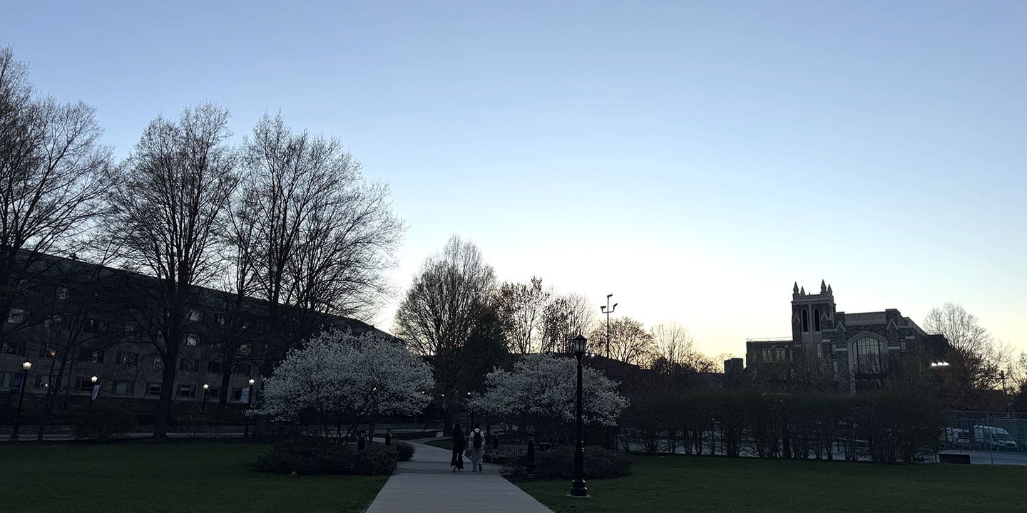 An almost deserted college campus at sunset with two people walking down a campus path.