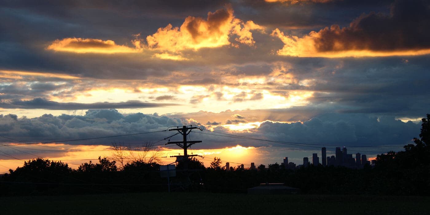 Image shows a sunset through clouds over an electrical pole.