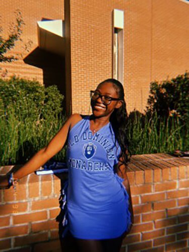 The blog author has long dark hair and is wearing glasses and a sleeveless light blue dress with the words Old Dominion Monarchs on it.