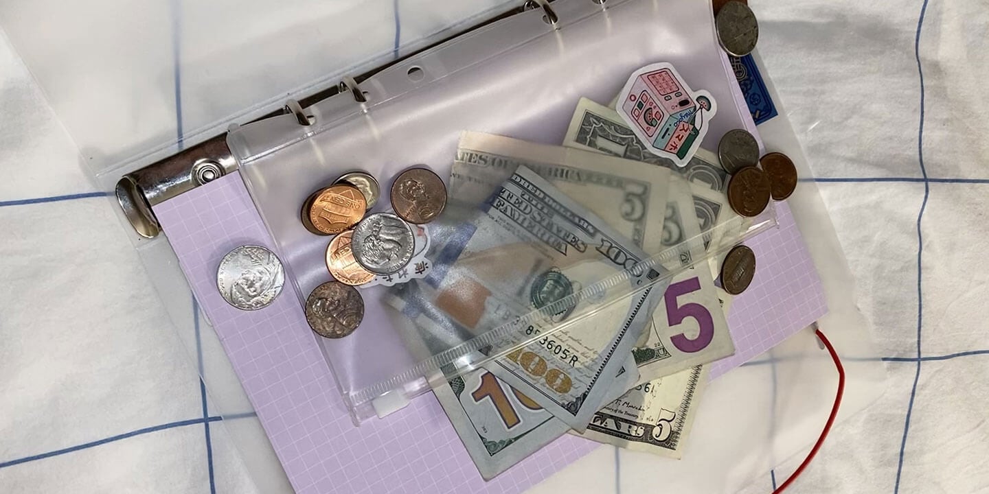 An open notebook with a clear pocket insert with cash in coins and bills.