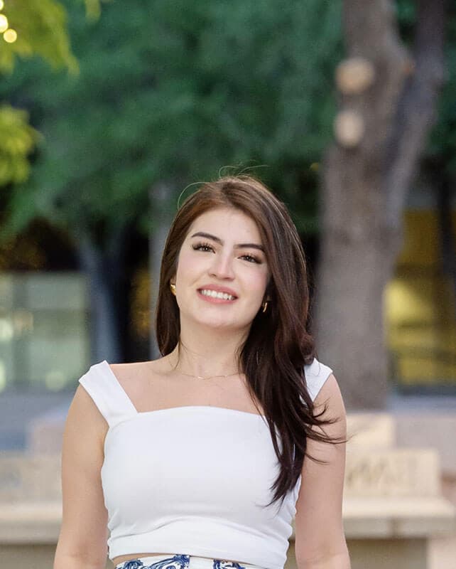 The blog author is outside and has long dark hair and is wearing a white top.