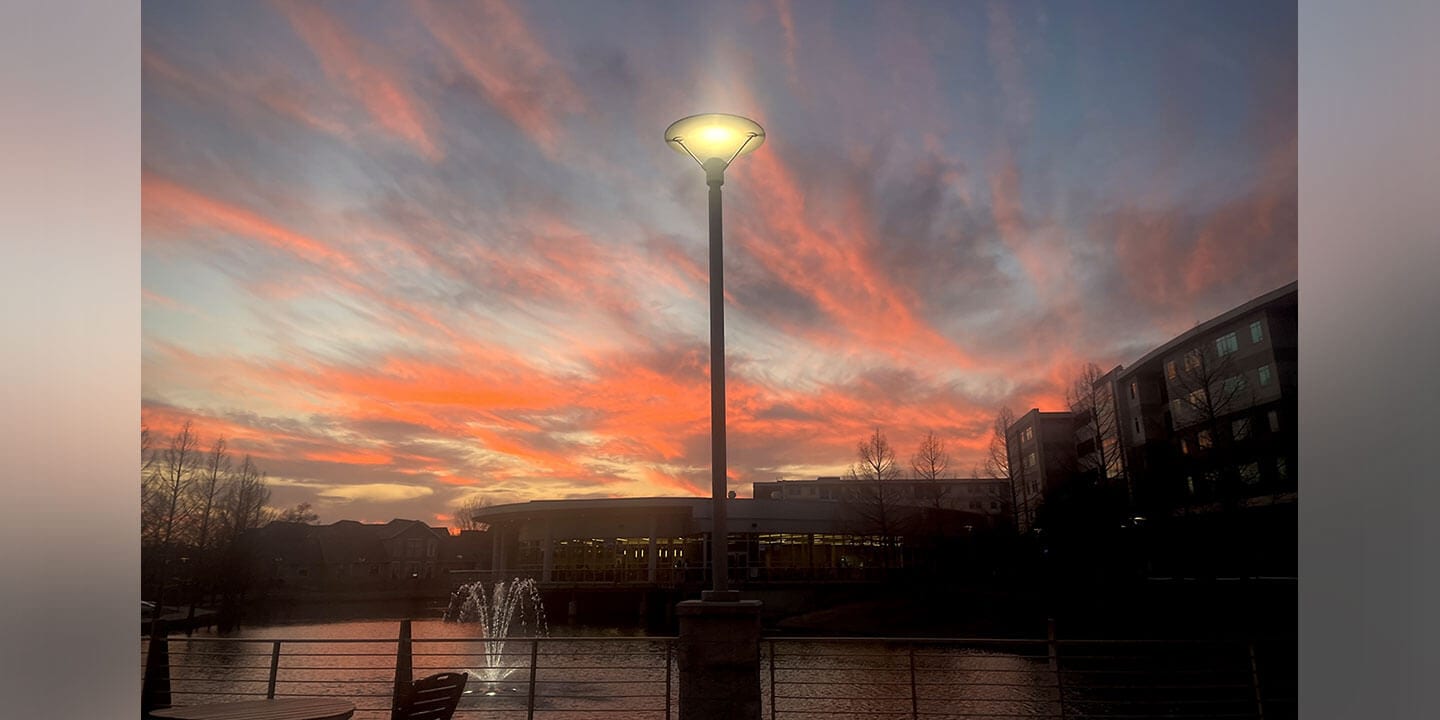 Image shows a lit lamp post at sunset surrounded by campus buildings