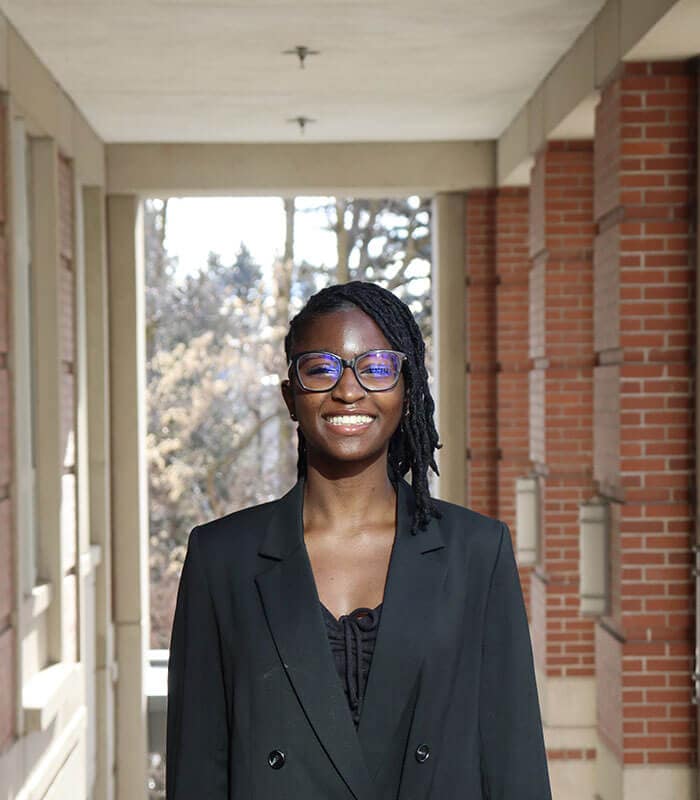 The blog author has medium length dark braids and is wearing glasses, a black shirt, and a black blazer.