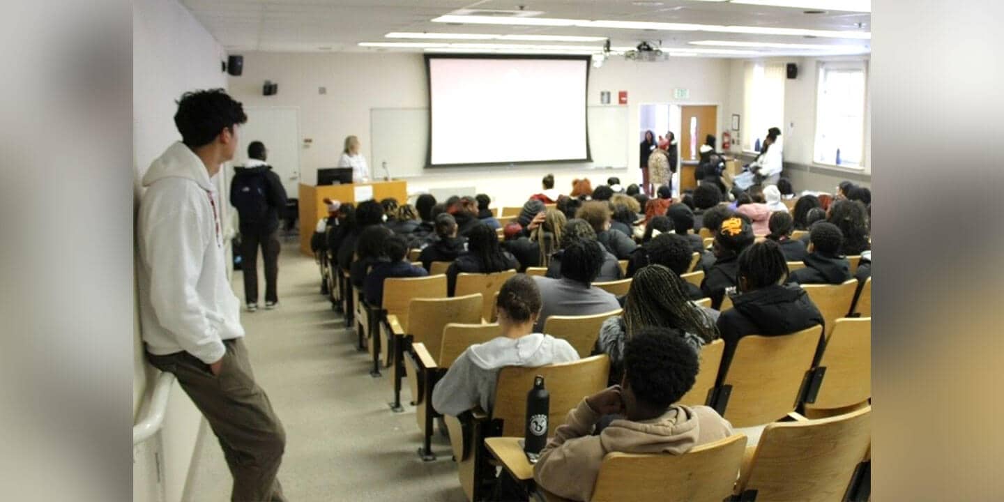 A classroom full of students and an instructor looking at a screen at the front of the room.
