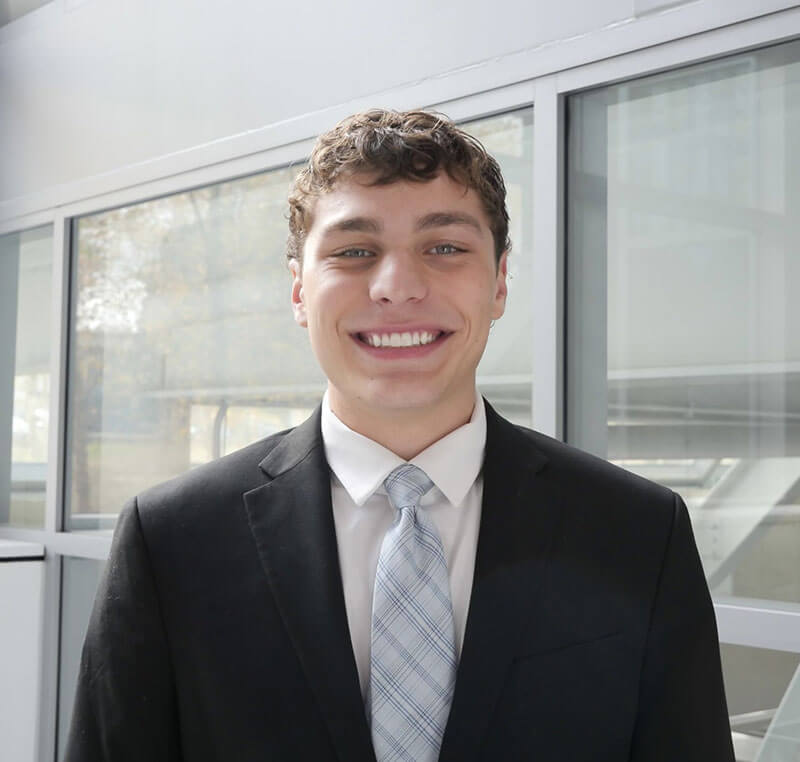 The blog author, Johnny, has short, brown curly hair and is wearing a black suit jacket with a white shirt and a light blue criss cross patterned tie.