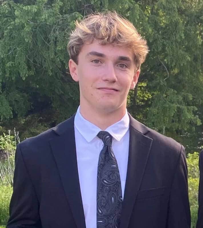 The blog author, Joshua, has sandy brown hair and is wearing a black suit jacket, white shirt, and a patterned tie. 