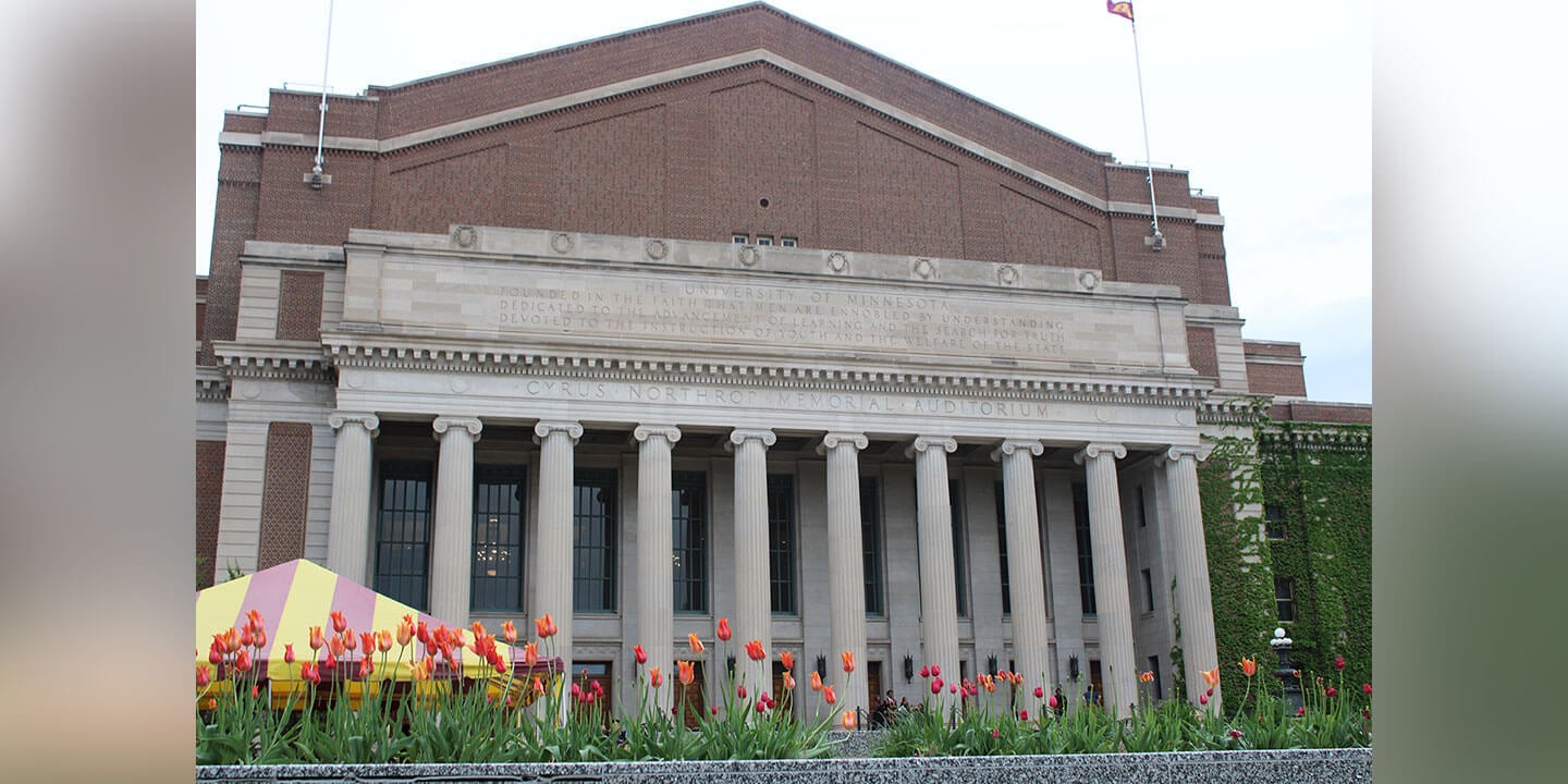 A grand brick building with columns with vibrant tulips in various colors in the foreground. A tent with red and yellow stripes is located off to the side.