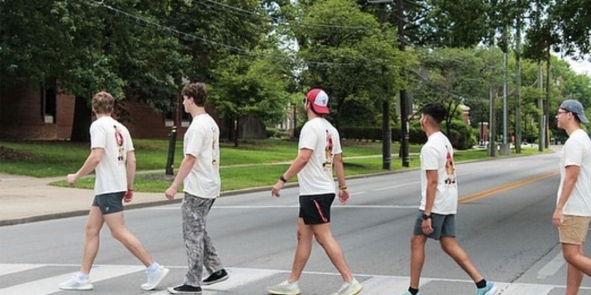 Image shows a group of five young men crossing the street in a marked crosswalk. They are dressed casually in t-shirts, shorts and athletic pants.