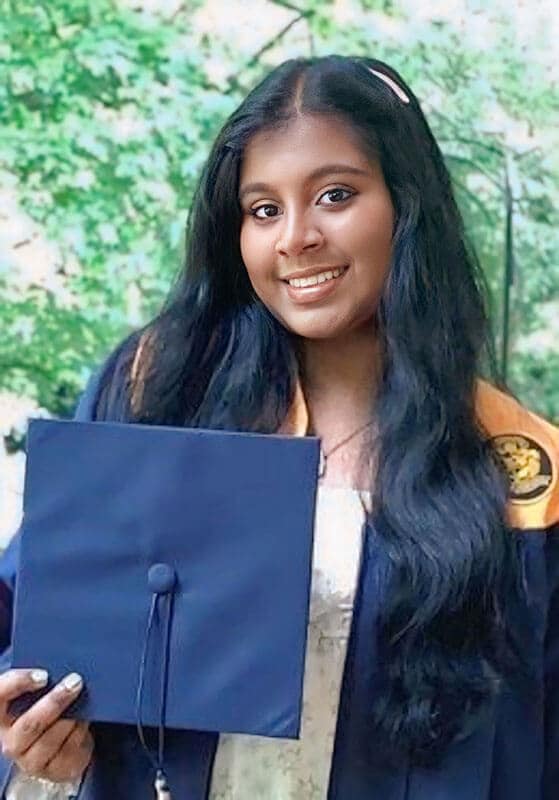 The blog author, Juanita, has long dark hair and is wearing a blue graduation gown over a white dress and is holding a blue graduation cap.