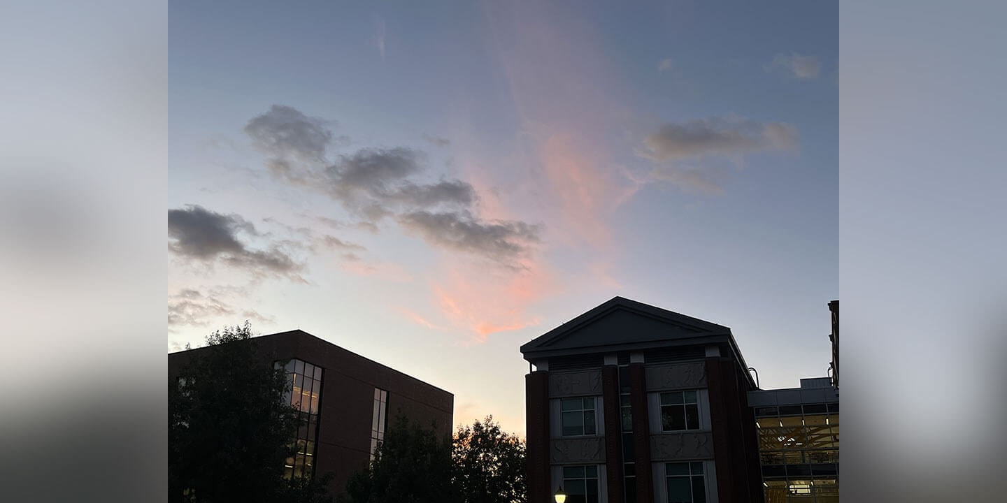 Image shows pretty pink and white clouds at sunset pictured over campus buildings.