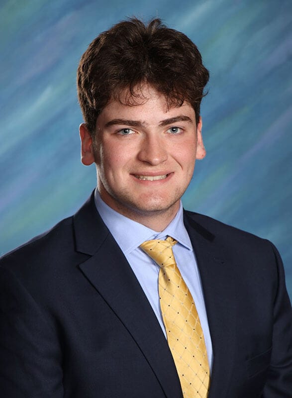 The blog author, Jonny, has dark hair and is wearing a dark blue blazer and a light blue dress shirt and a yellow tie.