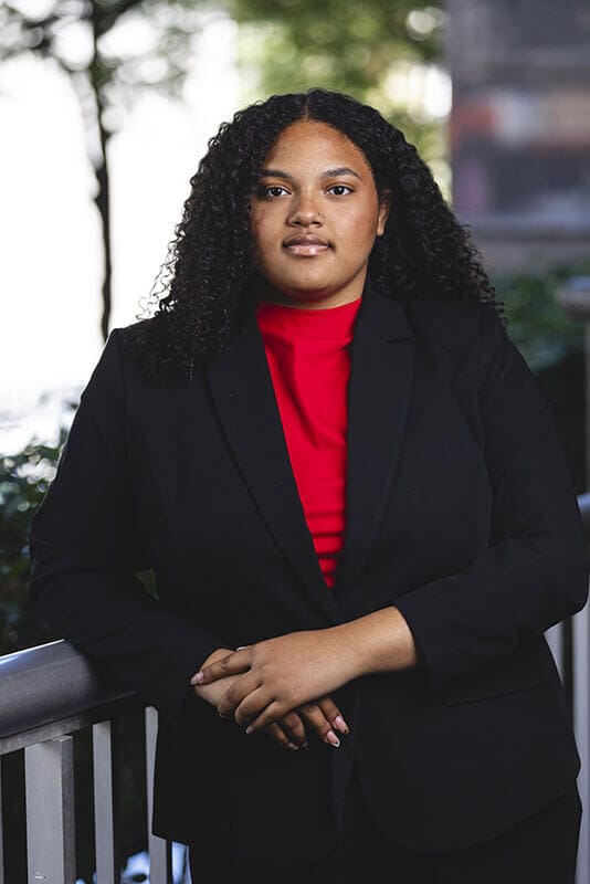 The blog author, Jordyn, has long, curly dark hair and is wearing a black suit jacket with a red blouse.