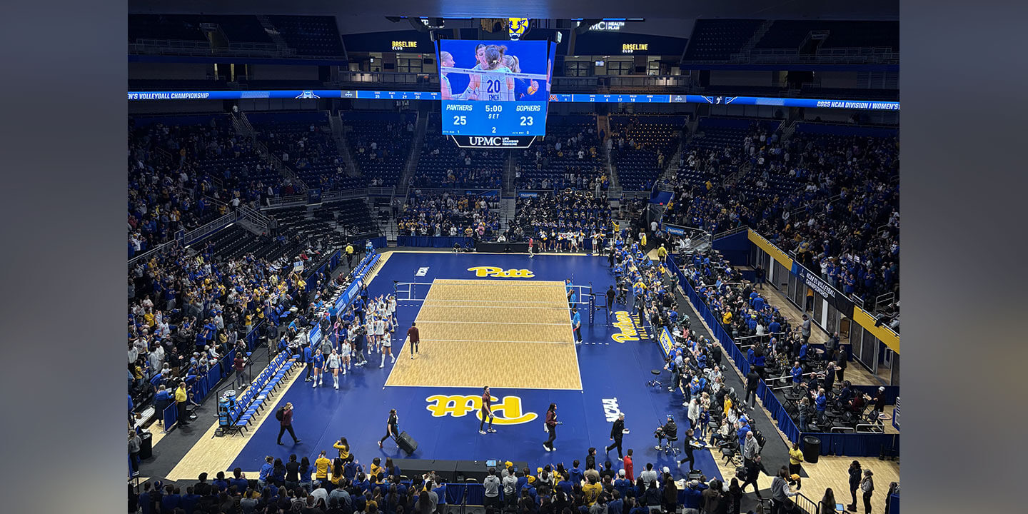 The scene shows a college volleyball match in a large indoor arena.