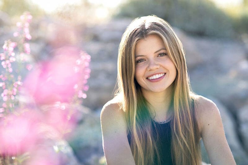 The blog author, Kathleen, is pictured outside alongside purple flowers and has long blonde hair and is wearing a black tank top.