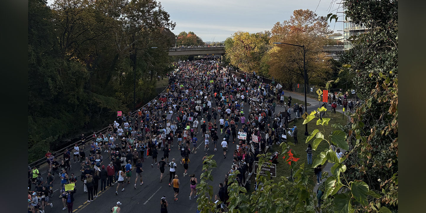 Image shows a marathon race in progress with runners on the course and spectators lining both sides.