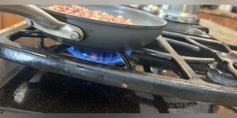 Bacon frying in a pan on a gas stove.