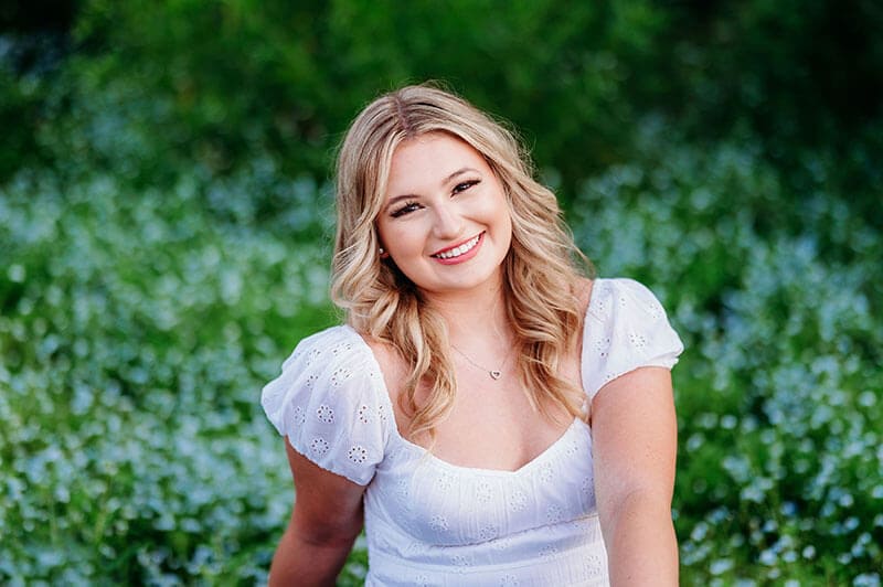 The blog author has long blond hair and is wearing a white eyelet patterned shirt with a small heart necklace.