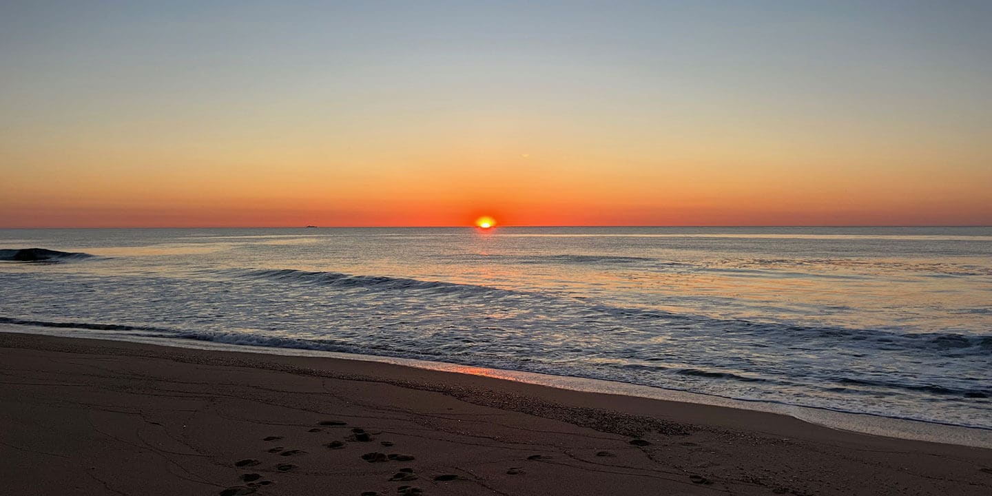 Photograph of a sunrise over the ocean with waves breaking on the beach.