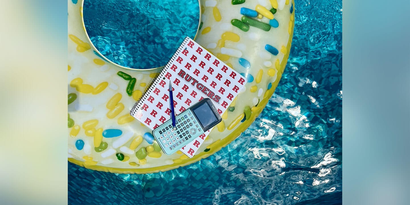 A spiral notebook, a calculator, and a mechanical pencil balanced on a pool float floating in a pool.