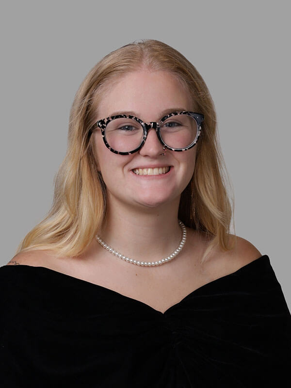 The blog author has long blond hair, dark glasses, is wearing a black shirt, and a pearl necklace.