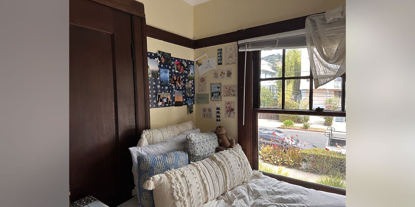A college dorm room featuring a large brown wardrobe, a bed with several throw pillows, and multiple pictures on the wall behind the bed.