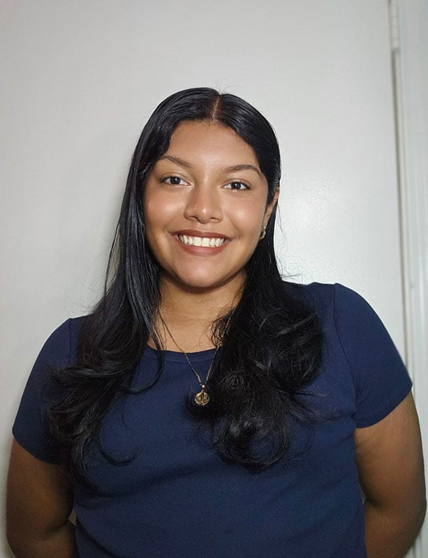 The blog author has long dark hair and is wearing a blue shirt with a gold necklace.