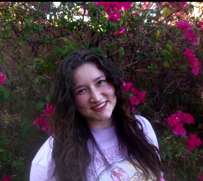 Blog author Meredith has long dark curly hair and is standing in front of a floral shrubbery.