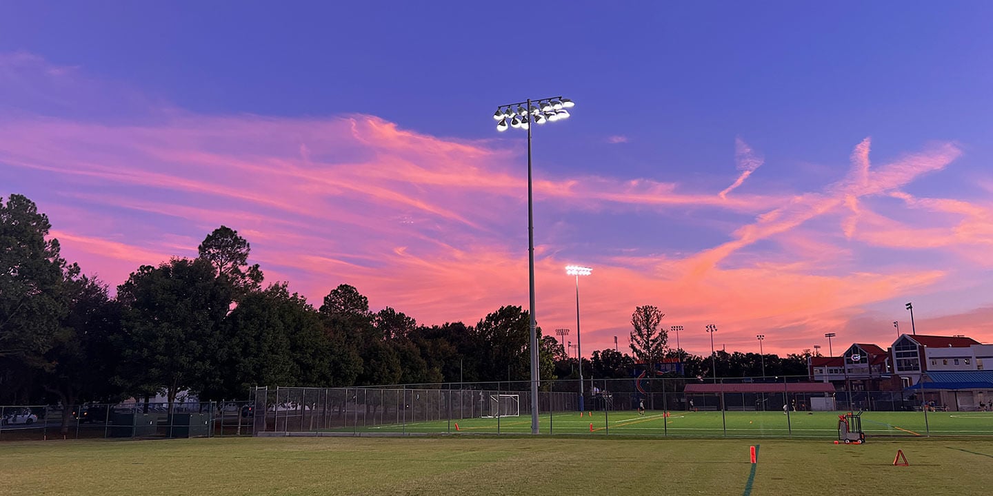 Athletic field at sunset with overhead lighting.