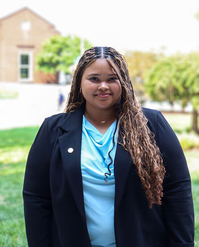Blog author Nia has long light brown curly hair and is wearing a dark navy blazer over a light blue top.