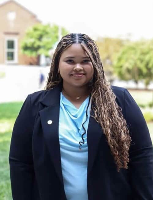The blog author, Nia, has long brown braids and is wearing a dark blue blazer and light blue top.
