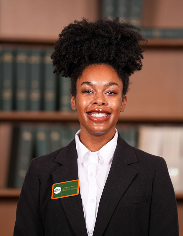 The blog author has dark hair styled in an updo, and she is wearing a dark blazer with a white shirt and a name badge. 
