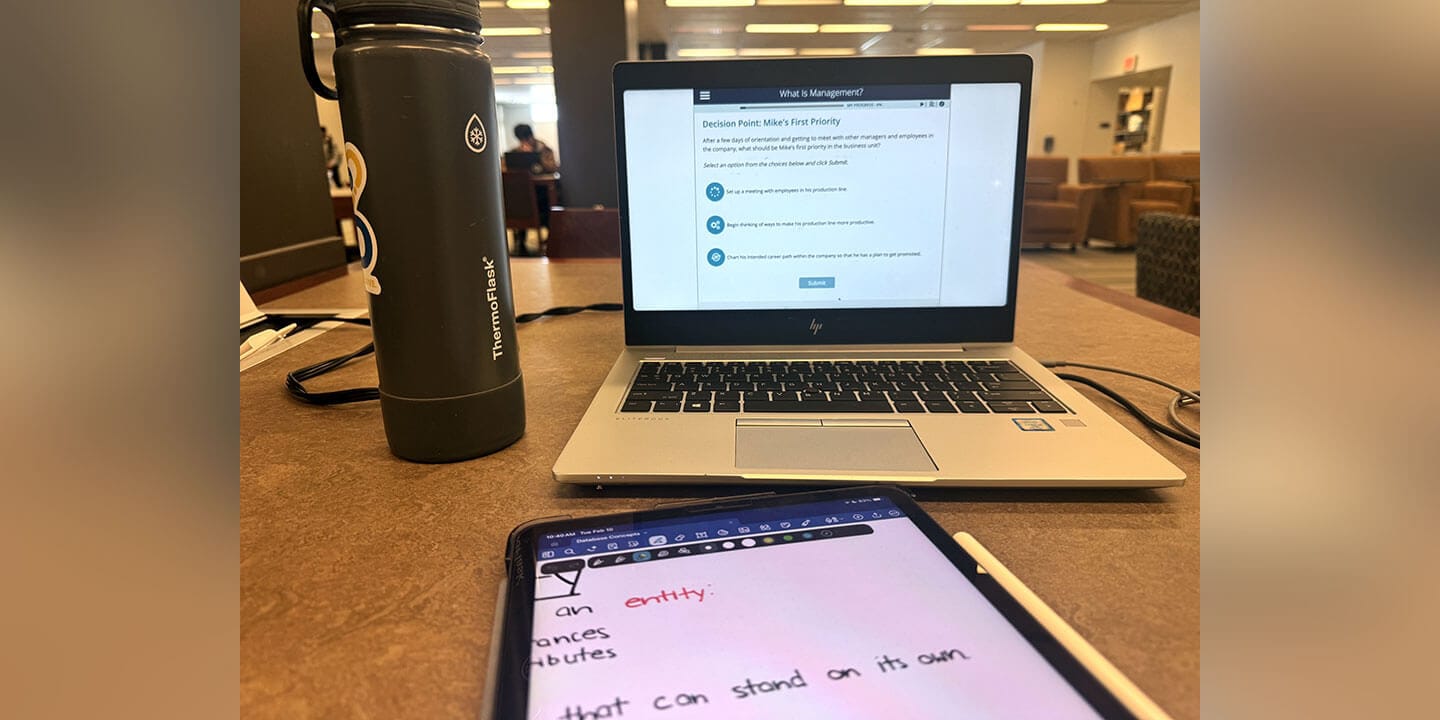 A water bottle, laptop, and tablet are all shown on a desk.