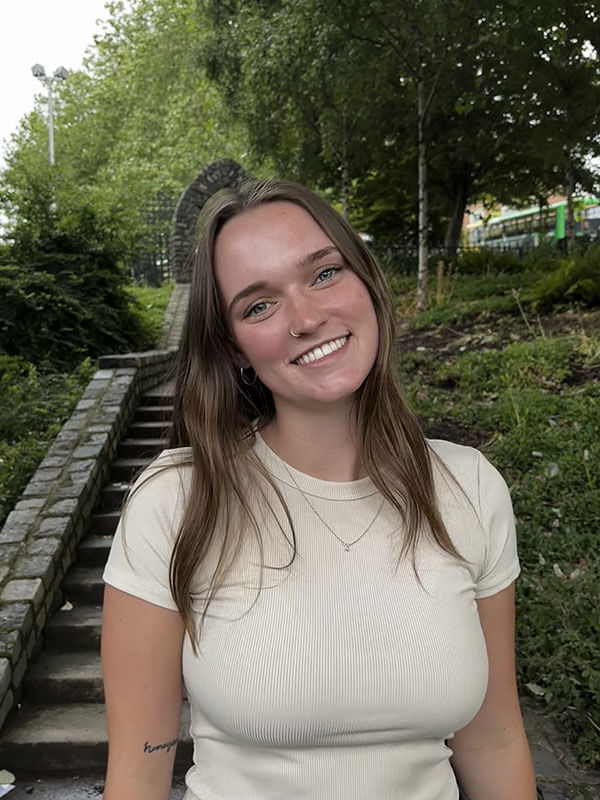 The blog author is pictured outside and has long light brown hair and is wearing a cream-colored t-shirt with a small necklace.
