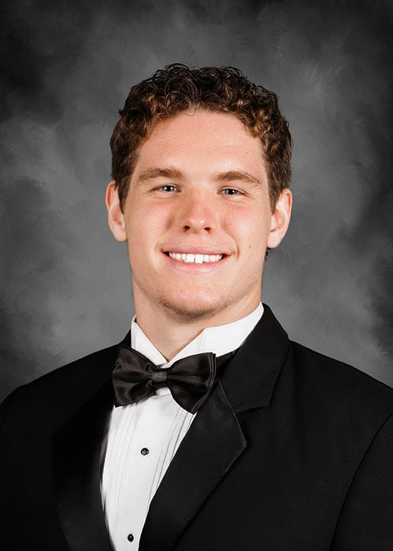 A studio headshot of blog author Silas. He has short curly hair and is wearing a tuxedo with a black jacket and bow tie over a white shirt.
