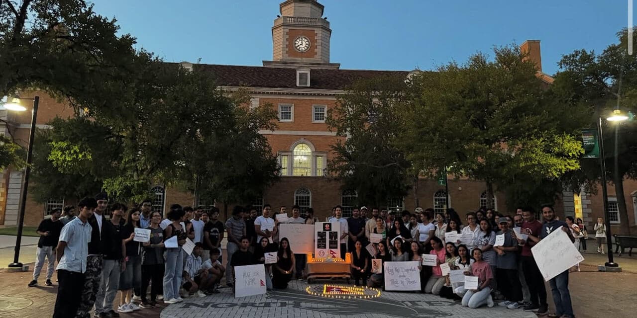 Group of students holding small signs in front of a campus building at a candlelight vigil. 