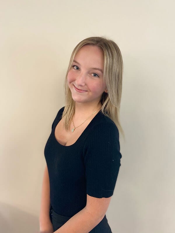 Blog author Alivia is standing in front of a white background. She had medium length blonde hair and is wearing a black short-sleeved top.
