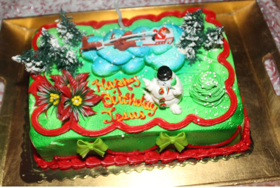 A birthday cake with the words ‘Happy Birthday Jesus’. It is decorated with green and red frosting and a snowman.