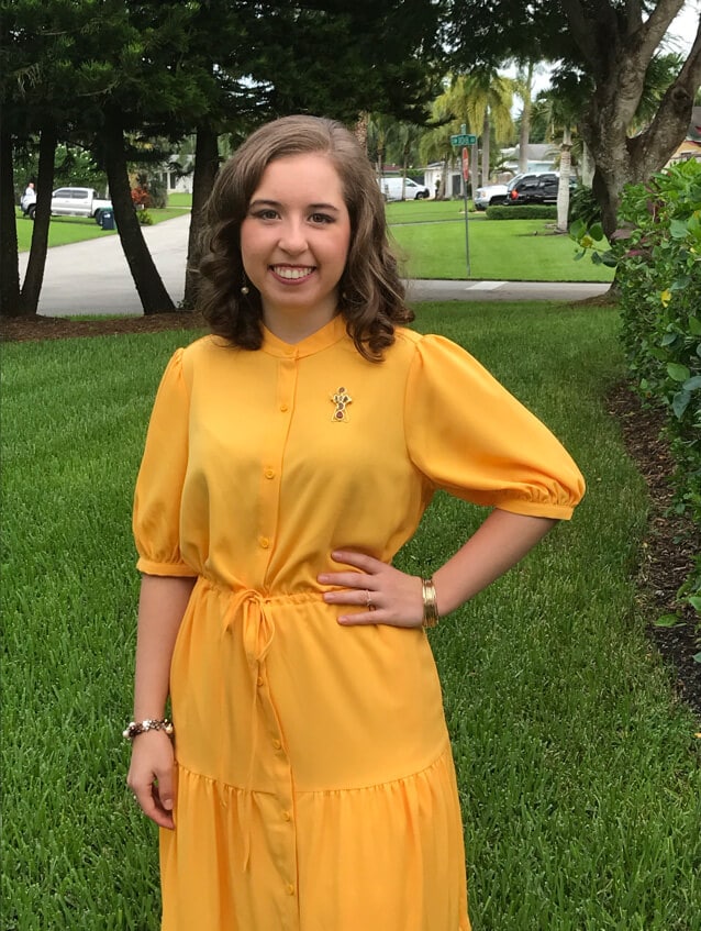 Blog author Ana Cooper is smiling and standing outside in a park. She has medium-length brown hair and is wearing a yellow-gold dress. 