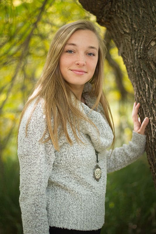 Blog author Alexis is standing by a tree. She has long blonde hair and is wearing a grey cowl neck sweater.