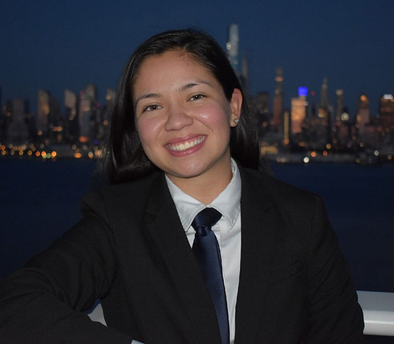 Blog author Angele Garcia is smiling and wearing a suit jacket, white shirt, and tie. A city skyline is behind her.