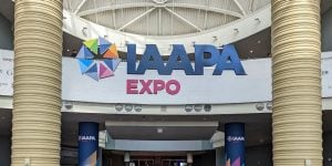 Large blue letters extended from a convention center ceiling that read: IAAPA expo. There is a large off-white column to either side of the letters.