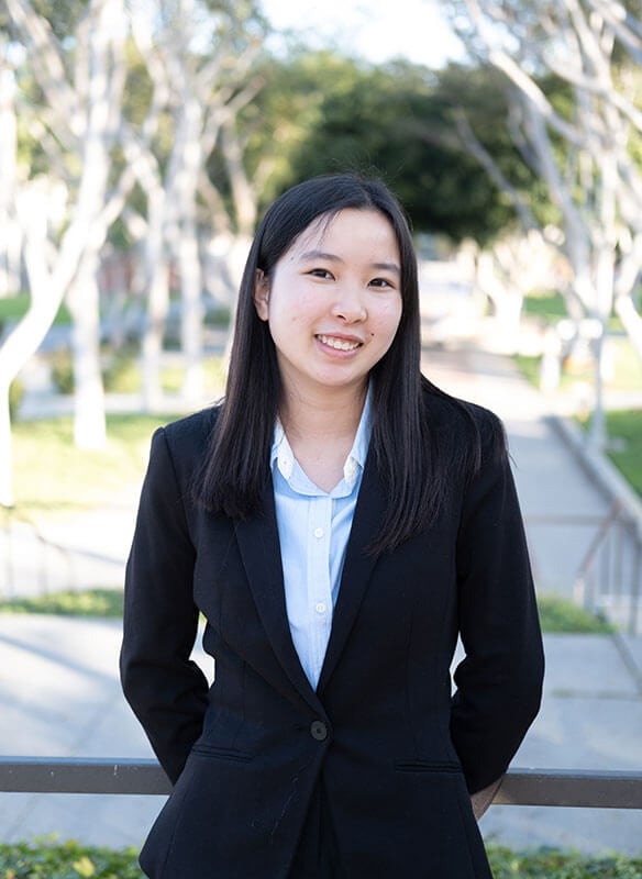 Blog author Alice Li is standing outside on a tree-lined path. She has medium length dark hair and is wearing a dark blazer over a white blouse.