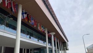 An academic building featuring white pillars and a collection of international flags hanging from the porch overhang.