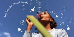 Student, Rachel Stennett blowing bubbles against a blue sky with heart and flower illustrations and the words 'Redefining Health and Beauty' in white.