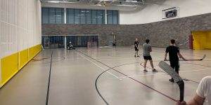 A group of college students playing indoor hockey in a campus gym.