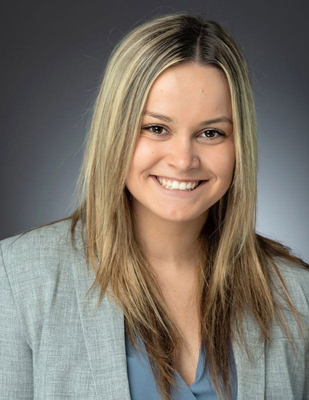 Blog author Courtney Lally is smiling in this studio headshot. She has long blonde hair and is wearing a grey blazer over a light blue blouse.