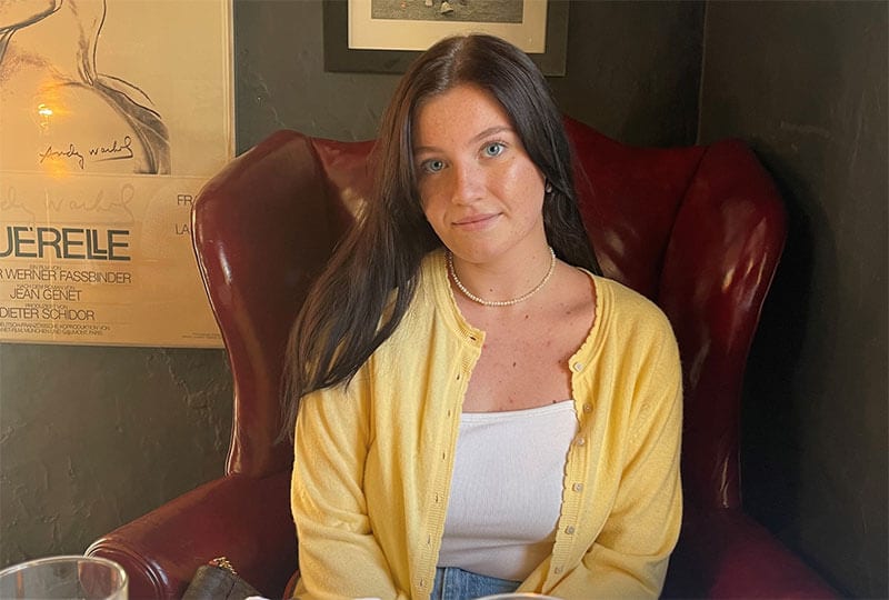 Blog author Casey Murphy is sitting in a leather chair. She has long dark brown hair and is wearing a yellow cardigan over a white t-shirt.