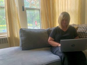 The blog author’s mom is sitting on a grey couch and working on a laptop computer.
