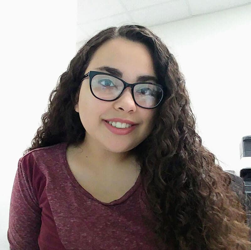 Blog author Keila Garza is wearing glasses and burgundy shirt. She has long dark wavy hair and is wearing glasses.