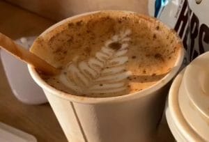 A latte in a white cup with a leaf design in the foam.